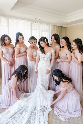 Bride in lace wedding gown surrounded by her beautiful bridesmaids adorned in light pink bridesmaid dresses.