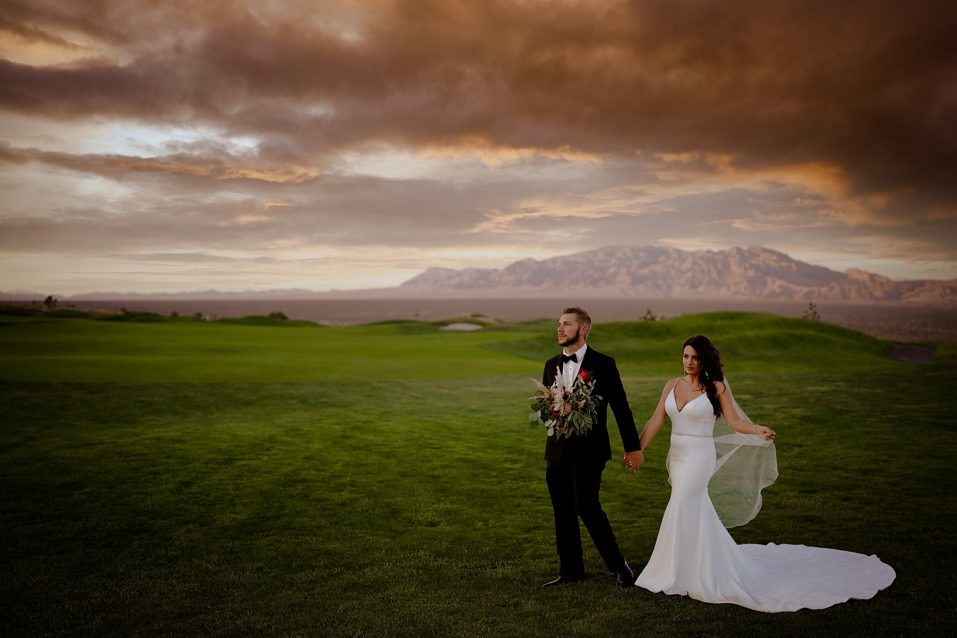 Couple poses in front of stormy desert sky on a lush lawn at Paiute Golf Club just outside Las Vegas