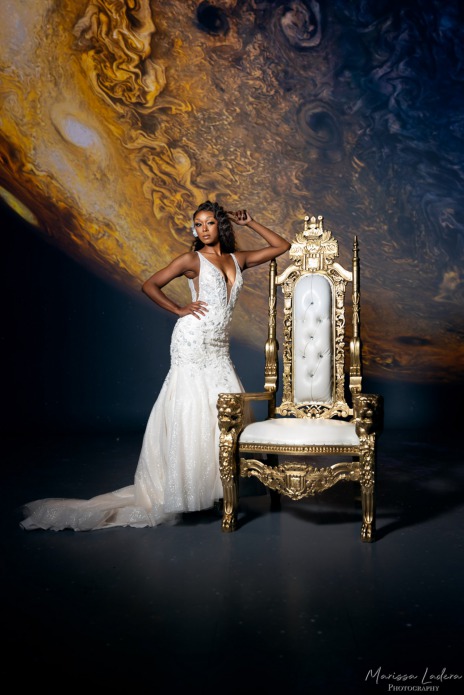 Gorgeous Bride in gown poses with Throne chair in front of a planetary background.