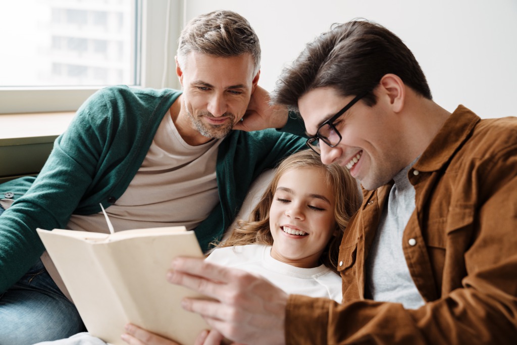 Happy,Gay,Parents,Reading,Book,Together,With,Their,Little,Daughter