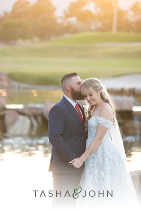 Tasha and John in their wedding finery embrace lovingly in front of a large outdoor water feature at a Las Vegas golf club venue