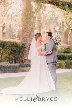 Kelli and Bryce look lovingly at eachother standing under a tree at their Las Vegas wedding. He looks handsome in his grey tuxedo and she looks lovely in her gown with a portrait neckline.