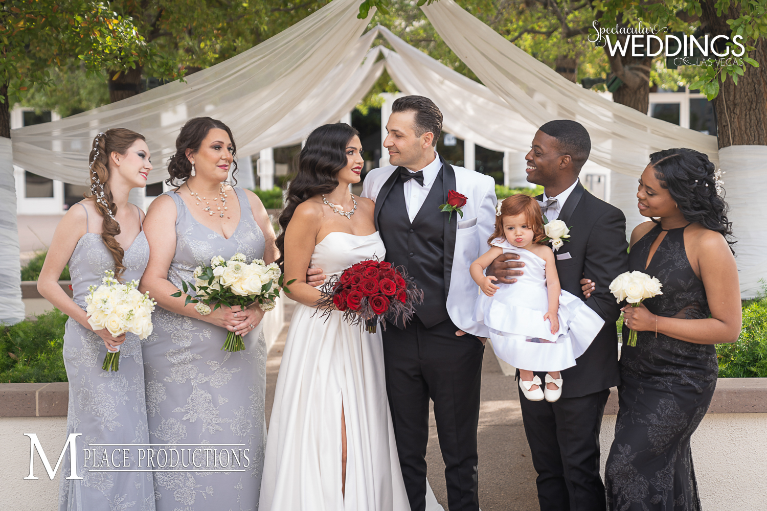 Happy couple stand surrounded by bridesmaids in black and silver and groomsman holding a cute flower girl at Emerald at Queensridge wedding venue in Las Vegas
